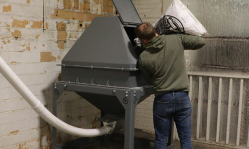Image of worker pouring grains into a hopper to begin grinding process.