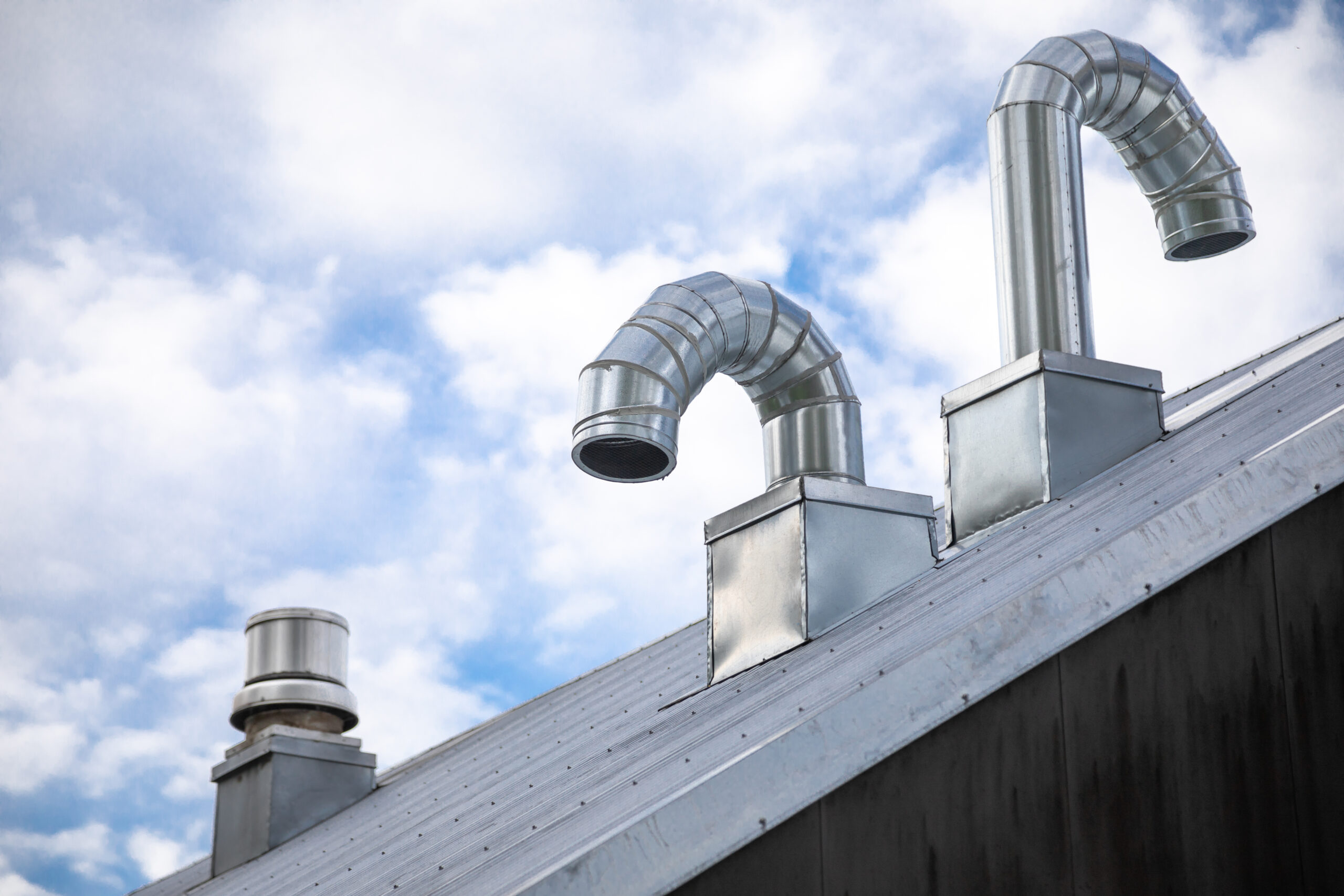 Side view of an aluminum chimney and ducting vents on the roof of an industrial building. 