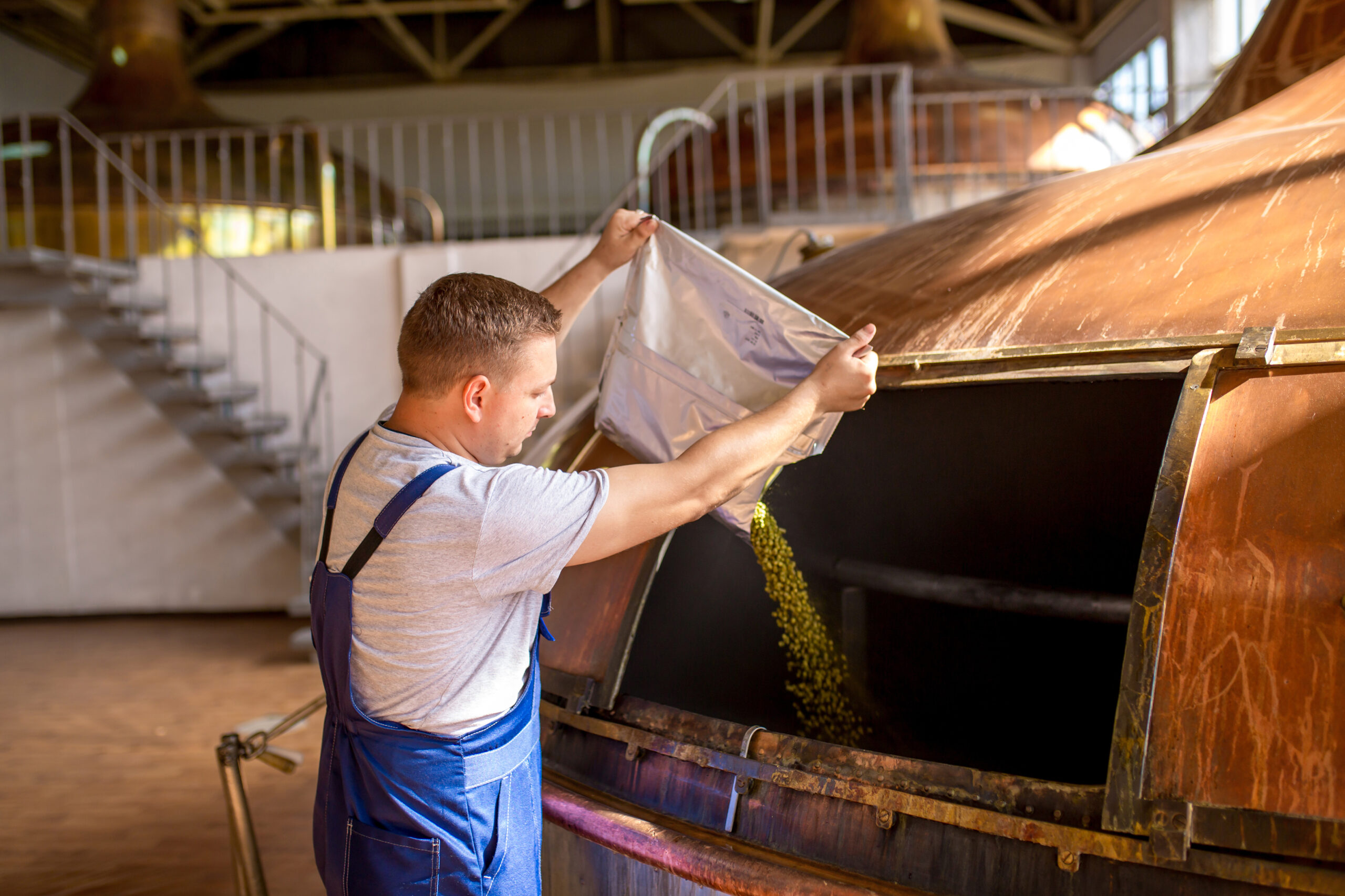 Worker pours ingredients into a brewing tank.