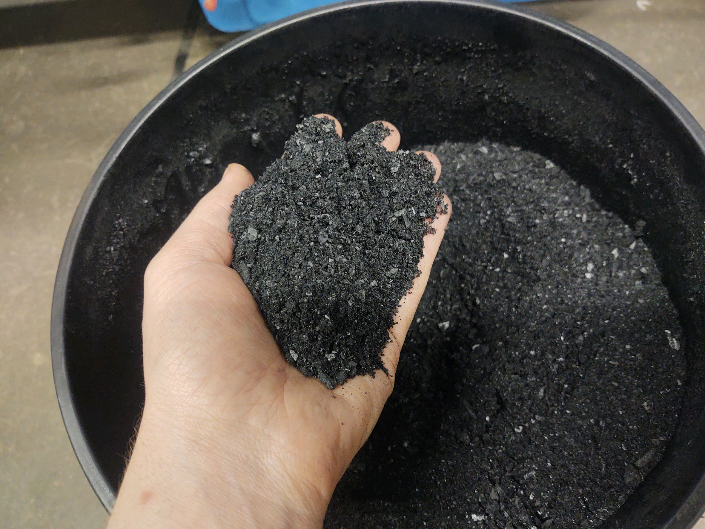 A hand holds up finely ground biochar over a black bucket. 