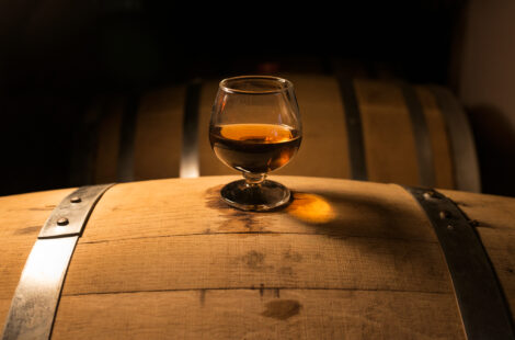 A glass of whiskey sits on top of a barrel.