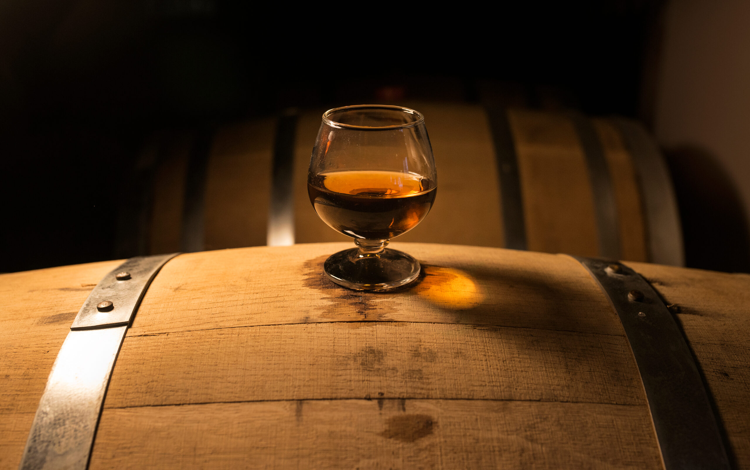 A glass of whiskey sits on top of a barrel.