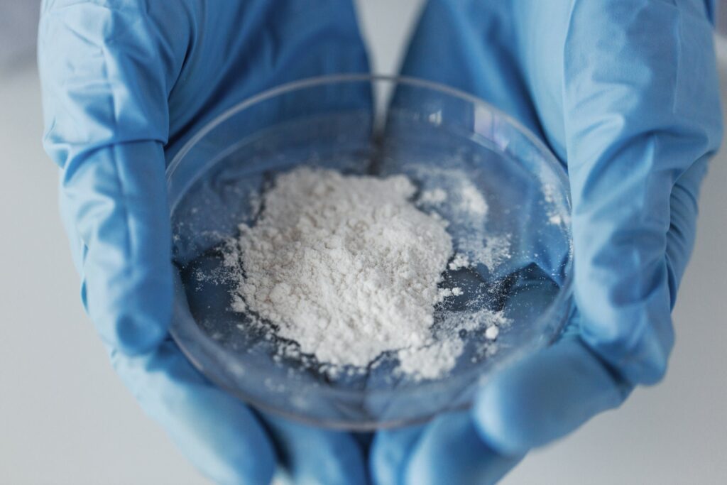 A person wearing blue gloves holds a clear dish of a finely ground white powder. 